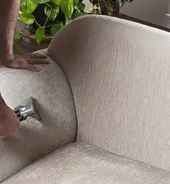 Professional upholstery cleaner deep-cleaning a fabric sofa with a handheld extraction tool and hose Kansas City, KS.